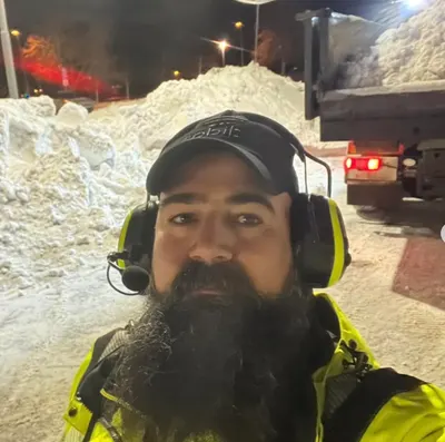 Akam Kader i gul varseljacka och hörselskydd vid ett nattarbete med lastbil i bakgrunden.